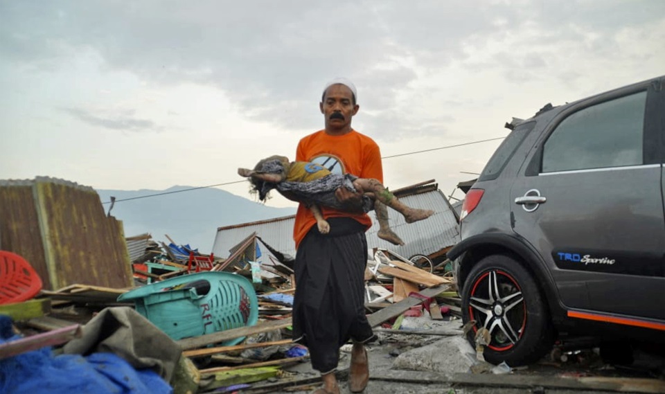 인도네시아 팔루에서 발생한 강진과 쓰나미로 1,600여명이 사망하고 수천명이 부상한 것으로 알려졌다. 사진은 한 남성이 지진과 쓰나미로 숨진 아이의 시신을 안고 걸어가고 있는 모습. / AP, 뉴시스