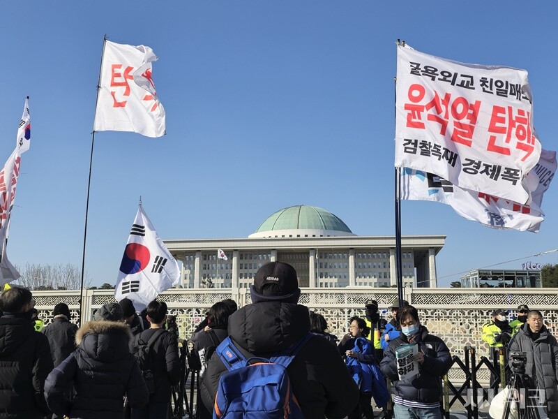 윤석열 탄핵소추안 의결이 예정된 14일, 이른 시간임에도 국회 앞엔 다양한 문구가 적힌 깃발을 들고 모여든 시민들로 북적였다. / 시사위크  