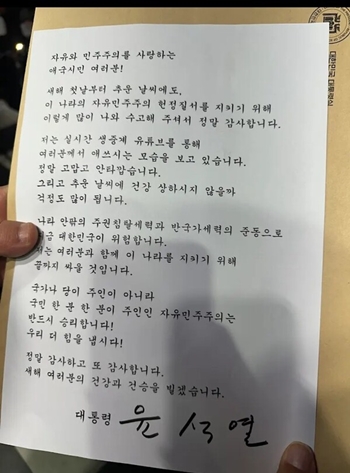 [서울=뉴시스] = 윤석열 대통령이 1일 오후 7시30분께 서울 용산구 한남동 대통령 관저 앞 도로에서 철야집회를 하는 지지자들에게 직접 서명한 새해인사 및 감사인사글을 전했다. / 사진=석동현 변호사 제공