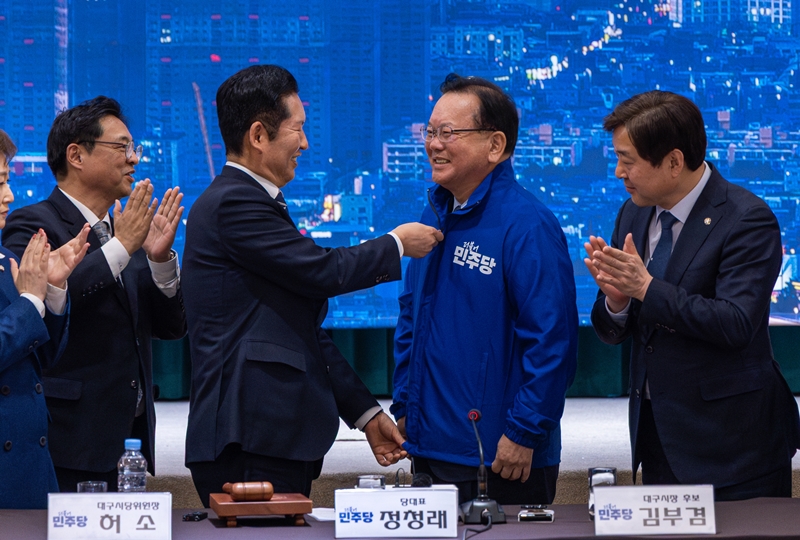 정청래 더불어민주당 대표가 지난 8일 대구 북구 인터불고 엑스코 호텔에서 열린 현장 최고위원회의에서 대구시장 후보인 김부겸 전 국무총리에게 당 점퍼를 입혀주고 있다. / 뉴시스