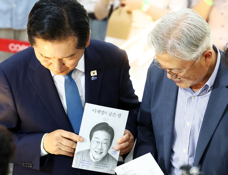 정청래 더불어민주당 전 대표가 24일 서울 강남구 코엑스에서 열린 2026 서울국제도서전 평산책방 부스에서 문재인 전 대통령을 만나 이재명 대통령의 저서를 들어보이고 있는 모습이다. (공동취재) / 뉴시스